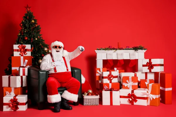 Retrato de su atractivo grasa funky sobrepeso alegre alegre Santa sentado en sillón viendo divertido programa de televisión canal de cambio riendo aislado brillo vivo brillante vibrante color rojo fondo — Foto de Stock