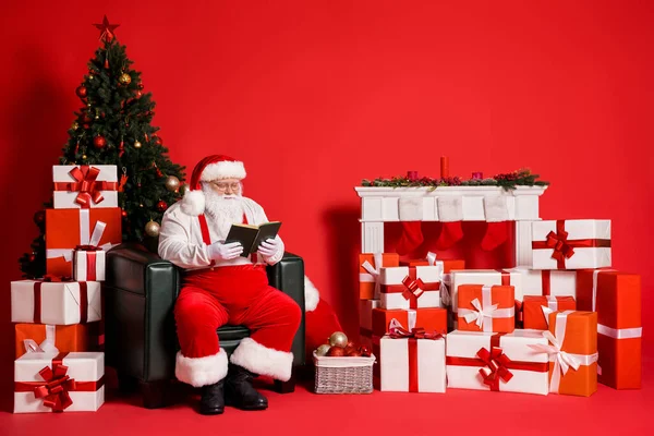 他的形象吸引人的肥胖超重聚精会神集中智慧的圣诞老人坐在扶手椅上看书度过佳节孤立明亮鲜亮的红色背景 — 图库照片