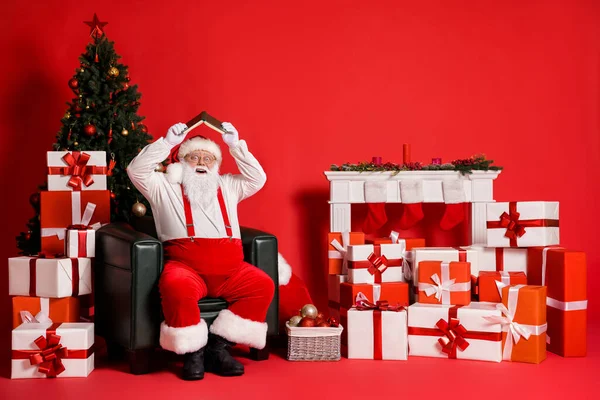 Portrait de son il attrayant graisse en surpoids funky enfantin joyeux heureux Père Noël assis dans le fauteuil tenant livre comme le toit ayant du plaisir isolé vif vif éclat vibrant fond de couleur rouge — Photo