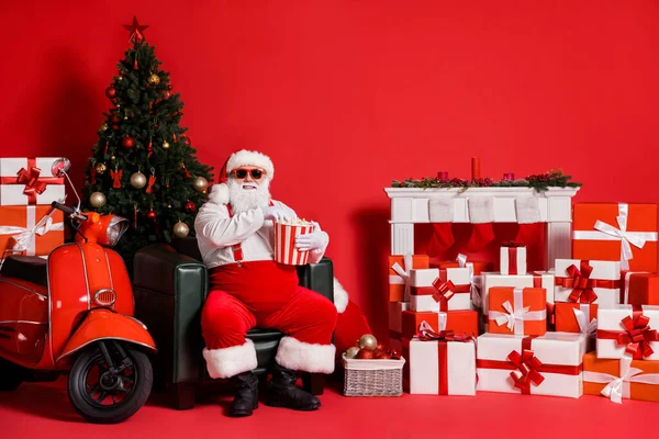 Güzel, şişman, şişman, neşeli Noel Baba koltukta oturmuş mısır yığını hızlı teslimat yığını hediye kutuları yiyor. — Stok fotoğraf