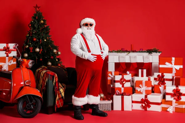 Noel Baba 'nın tam boy fotoğrafı, kırmızı renkli arka planda izole edilmiş, Noel Baba' nın büyük göbeğine dokunur. — Stok fotoğraf