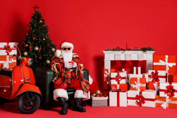 Foto em tamanho completo de santa claus sentar tampa da cadeira manta xadrez segurar caneca bebida quente isolado no fundo de cor vermelha com lareira x-mas — Fotografia de Stock