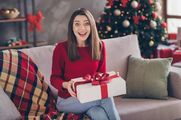 Şok olmuş bir kızın fotoğrafı kanepeye otur ve Noel hediyesini evde Noel süslemeleriyle birlikte al. — Stok fotoğraf