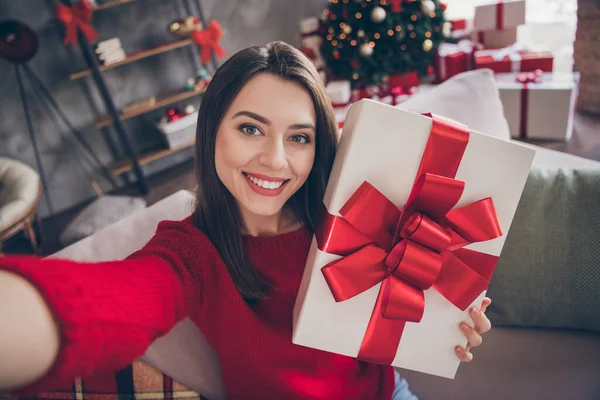 Pozitif kız hediye kutusunun fotoğrafı selfie 'yi evde Noel süslemesi ile birlikte oturma koltuğuna oturtur. — Stok fotoğraf