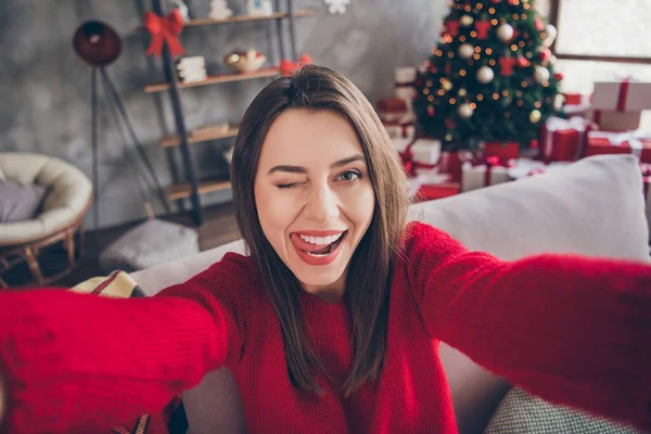 Φωτογραφία του θετικού κοριτσιού κάνει selfie κλείσιμο του ματιού γλώσσα λευκά δόντια κάθονται καναπέ στο σπίτι με χριστουγεννιάτικη διακόσμηση x-mas — Φωτογραφία Αρχείου
