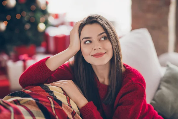 Φωτογραφία του minded κορίτσι κάθονται καναπέ όνειρο φορούν κόκκινο πουλόβερ στο σπίτι σε εσωτερικούς χώρους Χριστούγεννα πνεύμα Πρωτοχρονιά Σαββατοκύριακο γιορτή — Φωτογραφία Αρχείου