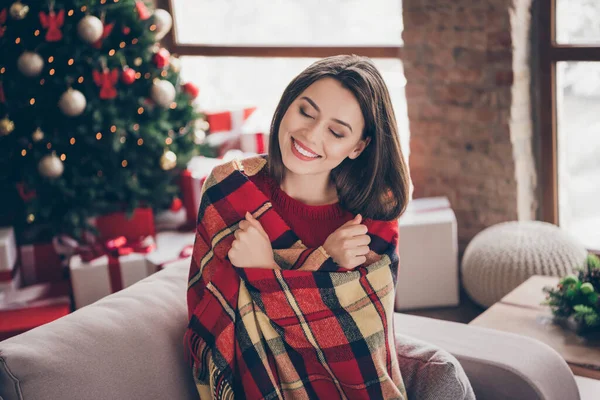 Foto de mulher encantadora sorriso brilhante envolto cobertor xadrez olhos fechados usar camisola vermelha na sala de estar decorada x-mas dentro de casa — Fotografia de Stock