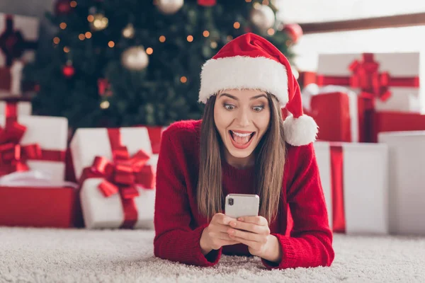 Close-up portrait of her she nice attractive amazed stunned cheerful glad ecstatic brown-haired girl lying on carpet floor using device browsing news wear festal hat in light house interior indoor — Stock Photo, Image