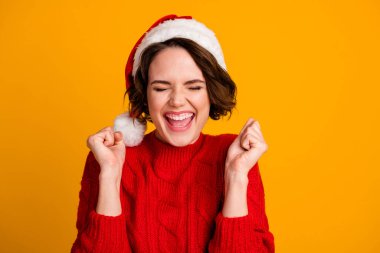 Closeup photo of funny crazy excited lady celebrate winter holidays raise fists eyes closed open mouth x-mas surprise wear santa cap red knitted sweater isolated yellow color background clipart