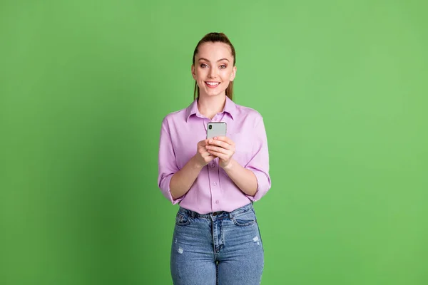 Foto van positieve meisje blogger gebruik smartphone genieten van sociale netwerk communicatie sms typen slijtage lila denim jeans geïsoleerd over groene kleur achtergrond — Stockfoto