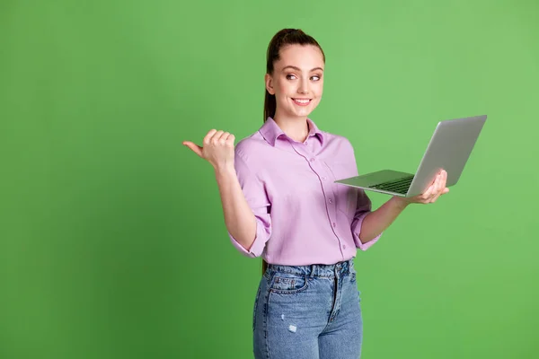 Photo de travail fille positive ordinateur portable à distance point pouce doigt copyspace indiquer réseau social promo porter violet lilas chemise jeans style denim isolé sur fond de couleur verte — Photo