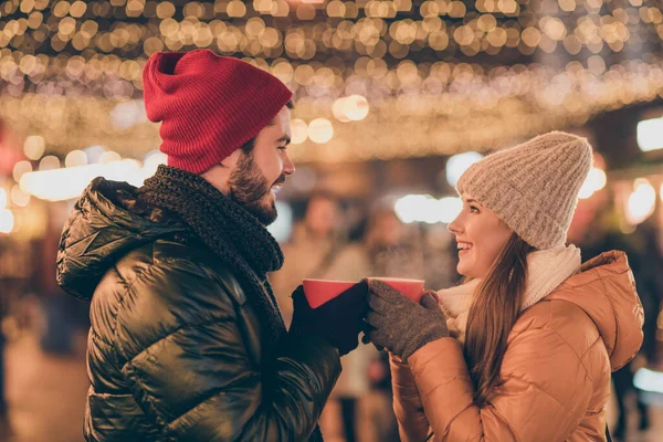 Photo of two people couple clink hot coffee beverage cup under evening x-mas tradition outside illumination wear season coats