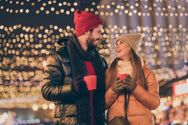 Фото ласкавої пари тримайте гарячу чашку напою під традицією Різдвяний вечір на відкритому повітрі під ілюмінацією шарф капелюха — стокове фото