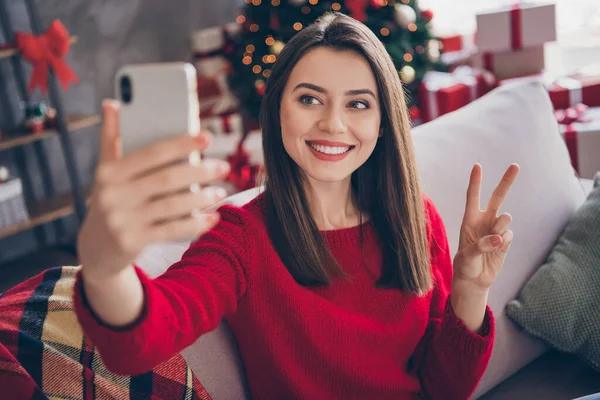 Фото позитивной девушки сделать селфи на смартфоне сделать V-знак в доме в помещении с рождественским орнаментом — стоковое фото