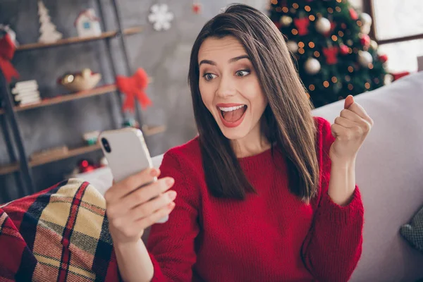Фото сумасшедшей девушки читать рождественские новости на смартфоне поднять кулаки сидеть диван в доме в помещении с новогодним украшением — стоковое фото