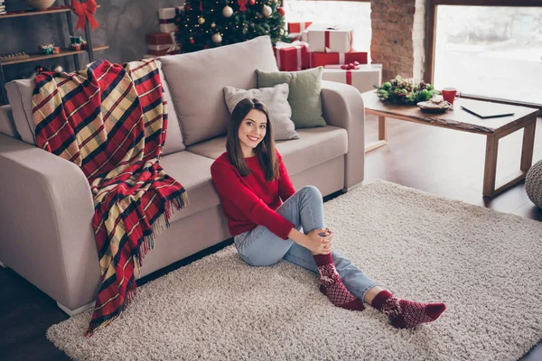 Fotografie roztomilé ženy sedět podlaha koberec pohovka mazlit nohy nosit červený svetr ponožky džíny v zdobené x-mas obývací pokoj uvnitř — Stock fotografie