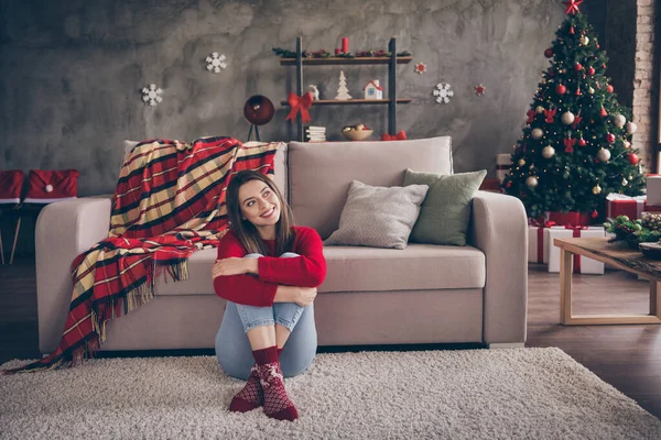 Foto de engraçado jovem menina confortável sentar sofá olhar para cima abraçar as pernas usar meias camisola vermelha jeans em decorado x-mas sala de estar dentro de casa — Fotografia de Stock