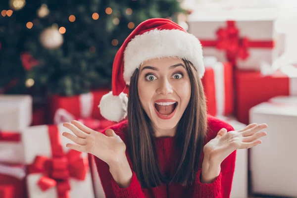 Foto de regalos impactados de chicas jóvenes manos boca abierta mirando fijamente desgaste santa headwear suéter rojo en decorado x-mas sala de estar en el interior — Foto de Stock