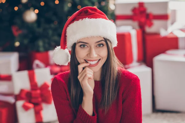 Foto de chica encantadora sentarse alfombra regalos dientes morder uñas desgaste santa gorra suéter rojo en decorado x-mas sala de estar en interiores — Foto de Stock