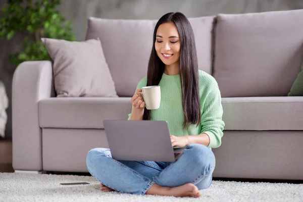 Pieno lunghezza foto di positivo coreano studente ragazza sedersi pavimento gambe attraversato piegato lavoro remoto laptop leggere documento relazione tenere tazza bevanda in casa al chiuso — Foto Stock