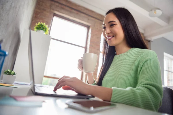 Low angle view profile side photo of positive ceo asian smart expert girl sir desk work remote laptop watch seminar drink beverage mug in house indoors