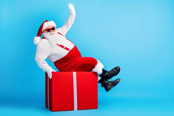 Lunghezza completa foto di grasso sovrappeso Babbo Natale con grande barba di stomaco sedersi scatola regalo rosso saluto x-mas partito indossare bretelle tuta da sole isolato colore blu sfondo — Foto Stock