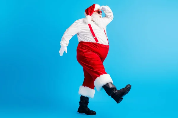 Full body profil boczny zdjęcie nadwagi tłuszczu Santa Claus z dużym brzuchem broda go copyspace wygląd x-mas Boże Narodzenie reklamy nosić szelki ogólny czapka izolowane na niebieskim tle — Zdjęcie stockowe