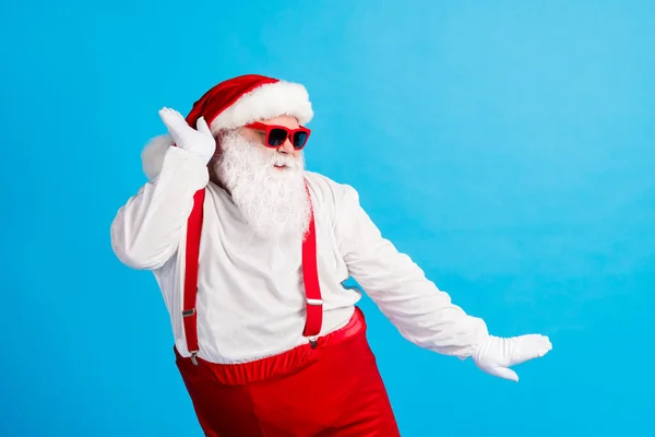 Photo of santa claus hipster tánc karácsony x-mas vidám party viselni piros sapka nadrágtartó overál napszemüveg elszigetelt felett kék színű háttér — Stock Fotó