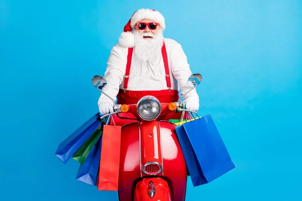 スタイリッシュな現代クレイジーホワイトグレーの髪ひげそりサンタクラスドライブの写真x-masクリスマススクーターホールドバッグを身に着けている赤い衣装サスペンダー全体が青の色の背景に孤立 — ストック写真