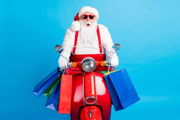 Incroyable blanc cheveux gris barbu santa claus conduire moto shooping centre commercial tenir sacs x-Noël Noël saison tradition affaire porter rouge costume bretelles salopettes isolé bleu couleur arrière-plan — Photo