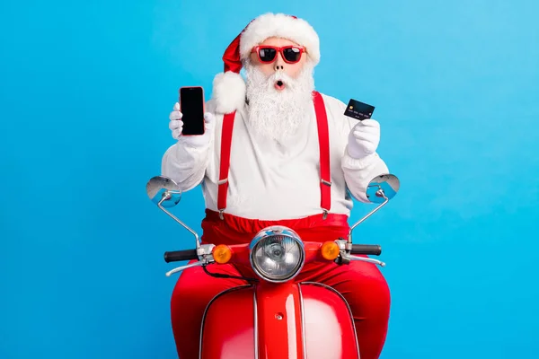 Büyükbaba Gri sakal sürücüsü eski motosiklet tutuş kartı boş uzay ekranı Noel Baba x-mas kostüm askısı güneş gözlüğü beyaz gömlek şapka izole mavi arka plan — Stok fotoğraf
