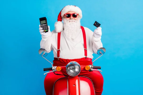 Beyaz, gri saçlı, Noel Baba, Noel Baba, Scooter sürücüsü, kredi kartı okuyucusu, mavi arka planda izole edilmiş kırmızı pantolon askısı kapağı giyiyor. — Stok fotoğraf