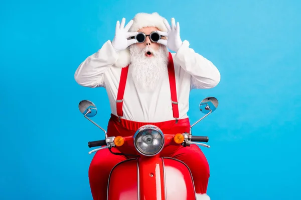 Foto van gekke verbaasd santa claus met baard rijden moderne motor x-mas kerst feest aanraken handschoenen bril dragen bretels overalls hoed geïsoleerd over pastel kleur achtergrond — Stockfoto
