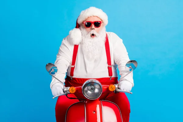Foto van verbaasd stijlvolle santa claus met witte baard rijden scooter snelle snelheid haast x-mas kerst feest dragen bretels overalls zonneglas geïsoleerd over blauwe kleur achtergrond — Stockfoto