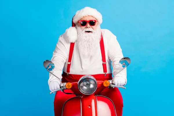 Fénykép nagyapa vezető szürke szakáll lovagolni gyors retro motorkerékpár mosoly viselet santa claus x-mas jelmez nadrágtartó napszemüveg fehér ing fejfedő kesztyű elszigetelt kék háttér — Stock Fotó