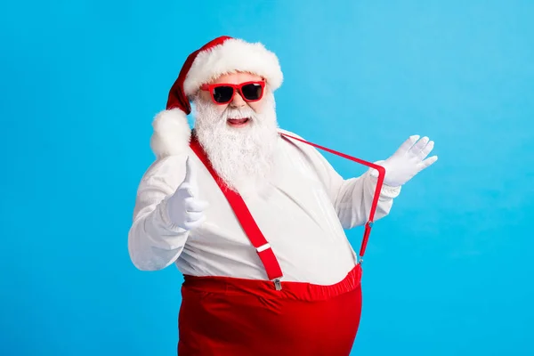 Photo of modern style santa claus with big abdomen pull suspender point index finger gloves x-mas christmas noel ads wear sunglass cap overalls pants isolated blue color background — Stock Photo, Image