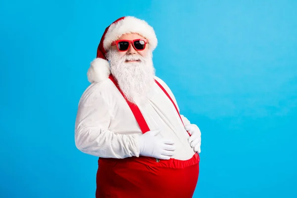 Φωτογραφία από τρελό υπέρβαρο santa claus αγγίζουν μεγάλη κοιλιά του απολαύσετε τα Χριστούγεννα Χριστούγεννα newyear παράδοση γιορτή φορούν πώμα τιράντες φόρμες απομονώνονται σε μπλε χρώμα φόντο — Φωτογραφία Αρχείου
