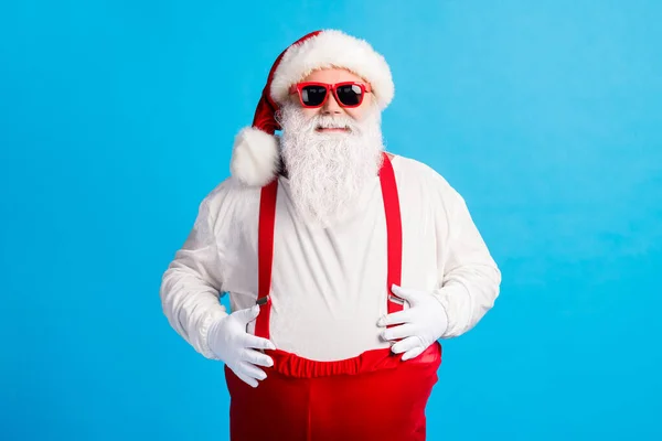 Foto van moderne trendy vet santa claus aanraken handen grote maag x-mas kerst noord-pole schepsel dragen hoofddeksel bretels overalls zonneglas geïsoleerde blauwe kleur achtergrond — Stockfoto