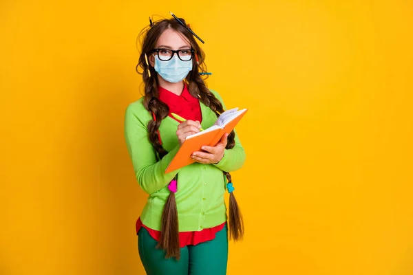 Retrato de atraente intelectual adolescente escrevendo ensaio fazendo lição de casa usar máscara isolada sobre cor amarela brilhante fundo — Fotografia de Stock