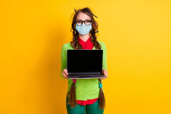 Retrato de menina atraente segurando em mãos demonstrando laptop tela desgaste máscara isolado cor amarela brilhante fundo — Fotografia de Stock