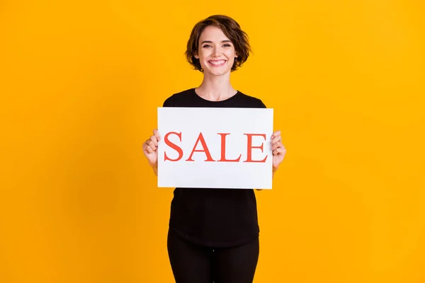 Porträt von attraktiven fröhlichen Mädchen hält in der Hand Papier Plakat Verkauf Werbung isoliert über helle gelbe Farbe Hintergrund — Stockfoto