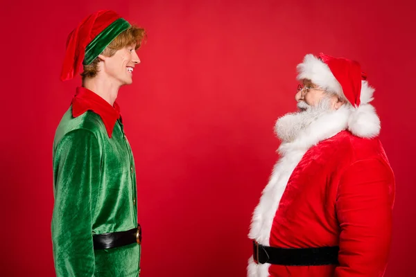 Photo de profil de deux personnes santa claus elfe regarder l'autre usure x-mas costume manteau casque isolé couleur rouge fond — Photo