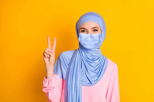 Close-up retrato de agradável atraente alegre muslimah senhora mostrando v-sinal vestindo máscara facial azul isolado sobre cor amarela brilhante fundo — Fotografia de Stock