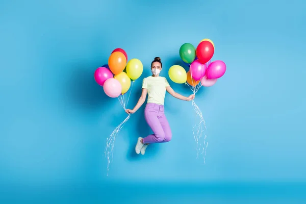 Volledige foto van meisje met stapel kleurrijke luchtballonnen springen hoge slijtage masker geïsoleerd op levendige blauwe kleur achtergrond — Stockfoto