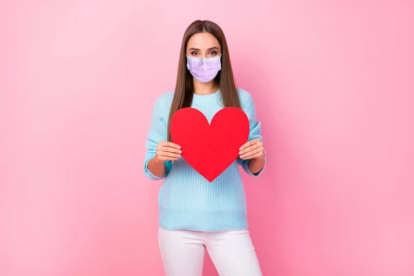 Foto van dame houden groot papier rood hart slijtage masker gebreid blauw trui witte broek geïsoleerde pastel roze kleur achtergrond — Stockfoto