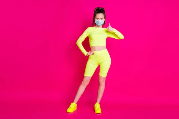 Foto de cuerpo entero de mujer joven vestida ropa deportiva máscara mano pulgar hacia arriba brazo cintura aislado color rosa fondo — Foto de Stock