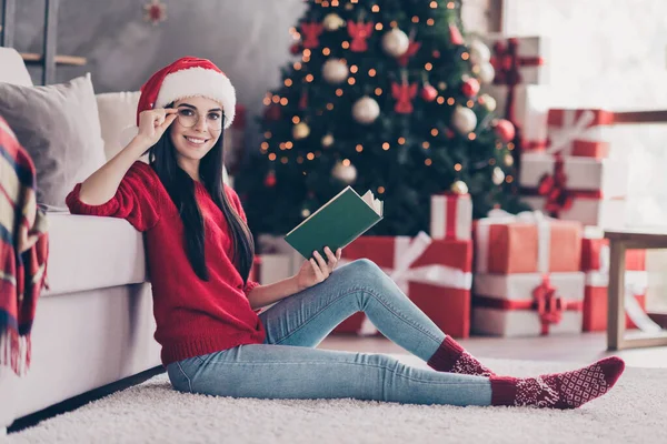 Helkroppsfoto av smart flicka sir matta läsa bok bära tomte klo hatt tröja i huset inomhus med jul jul julklappar — Stockfoto