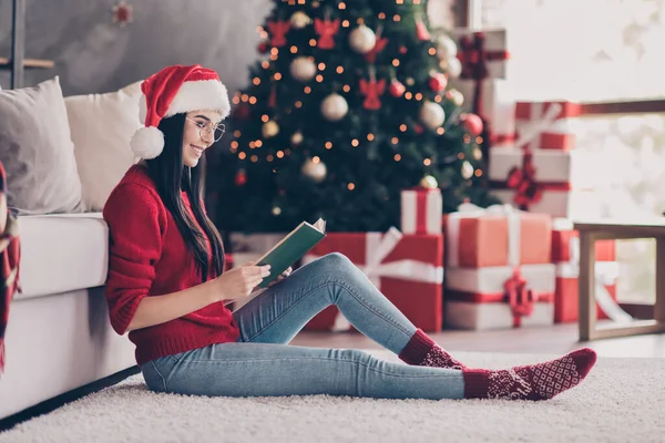 Повний розмір профілю фотографія дівчини в ковпачку Санта Клауса читати книгу сидячий килим в будинку з різдвяним прикрасою — стокове фото