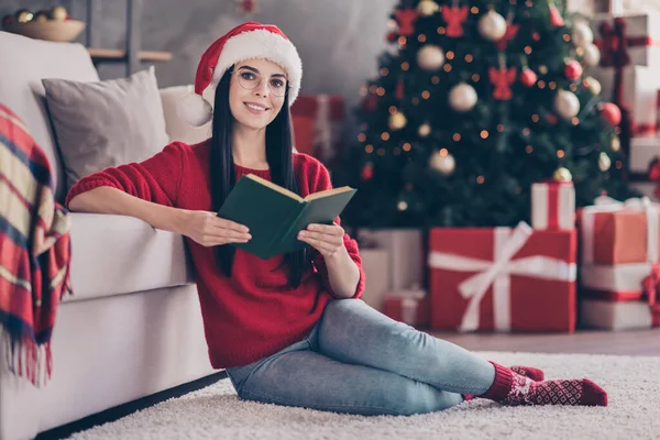 Full length photo of girl wear santa claus cap sit carpet read book in house indoor with x-mas christmnas decoration — Φωτογραφία Αρχείου