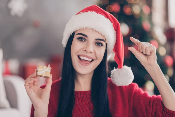 Chica positiva en santa claus sombrero celebrar pequeña caja de regalo medir los dedos en la casa en el interior con Navidad x-mas borlas — Foto de Stock